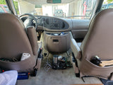 Inside an RV rental Ford van: dashboard, front seats, and floor with a power inverter & supplies for travel.