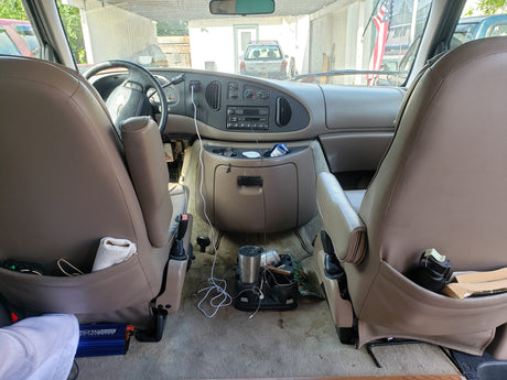Inside an RV rental Ford van: dashboard, front seats, and floor with a power inverter & supplies for travel.