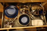 RV rental kitchen drawer: neatly organized dark blue plates, bowls, stainless steel pots, pans, and a measuring cup.