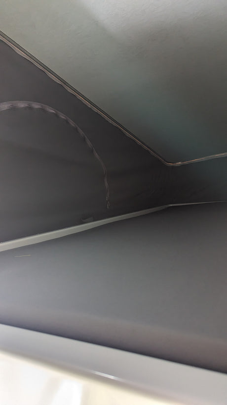 RV rental interior: Looking up at the ceiling and dark grey fabric walls with trim. A hanging zipper suggests a pull-down blind.