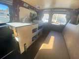 Cozy RV rental interior with a custom kitchenette, Dometic fridge, and comfortable bench seating in a camper van.
