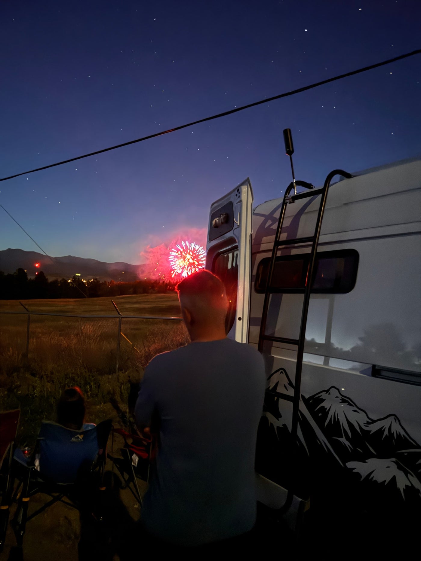 Night scene: Two people by an RV rental watch dazzling fireworks illuminate the mountain skyline and starry sky. — photo 4