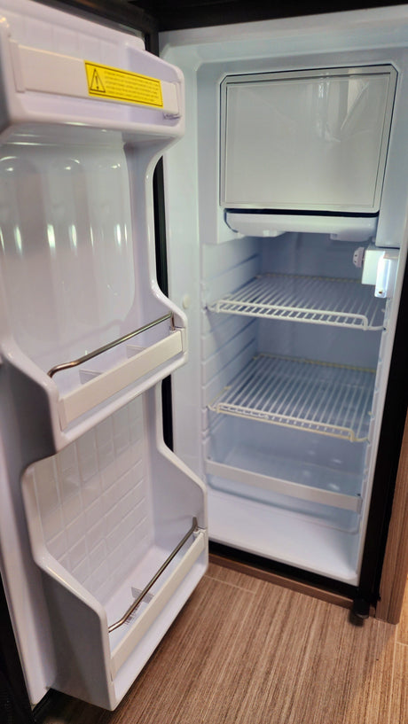 Clean and empty compact refrigerator with freezer in an RV rental, featuring wire shelves and door storage.