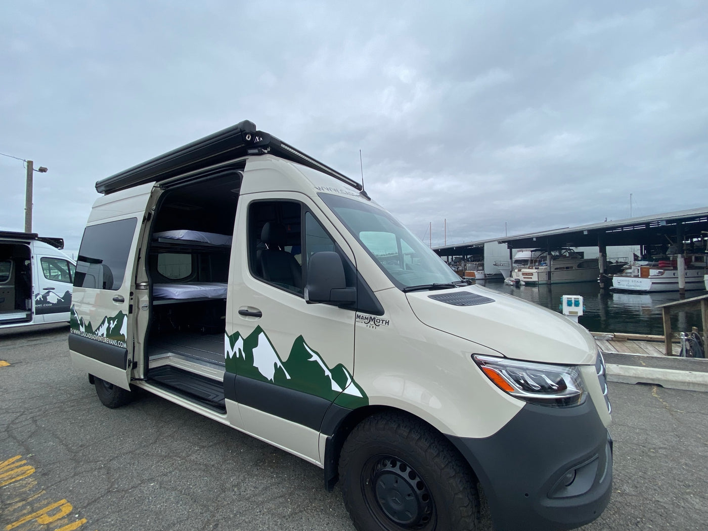 This custom Mammoth adventure van, an RV rental, with bunk beds inside, is parked by boats at a marina. — photo 3