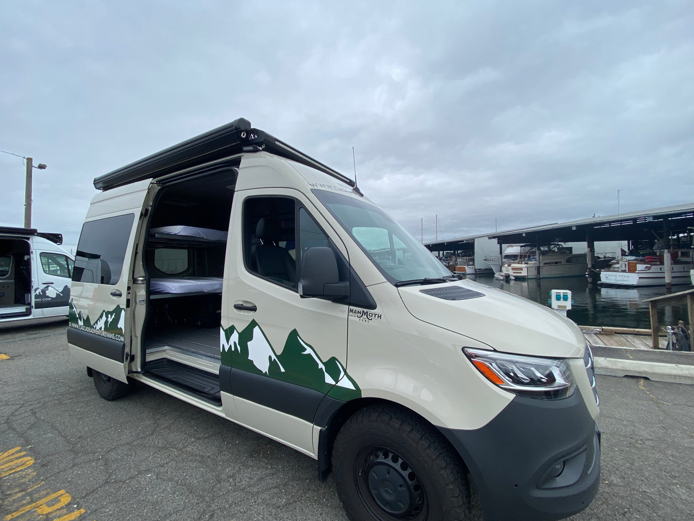This custom Mammoth adventure van, an RV rental, with bunk beds inside, is parked by boats at a marina.