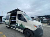 This custom Mammoth adventure van, an RV rental, with bunk beds inside, is parked by boats at a marina.