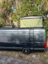 This dark gray RV rental camper van, equipped with a Trusthmade rooftop tent and Dometic unit, has a side ladder.