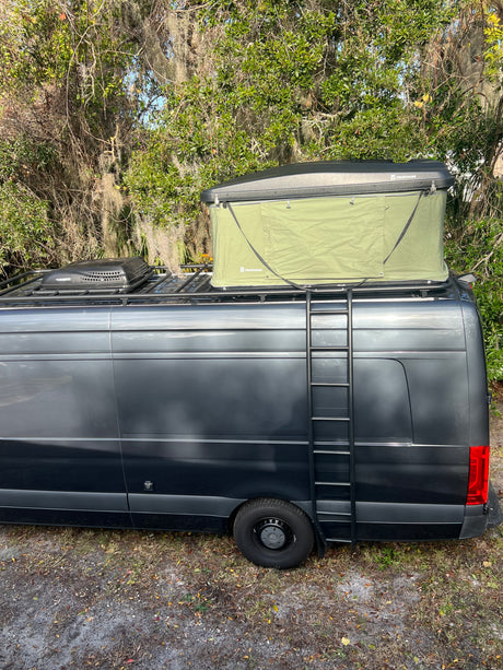 This dark gray RV rental camper van, equipped with a Trusthmade rooftop tent and Dometic unit, has a side ladder.