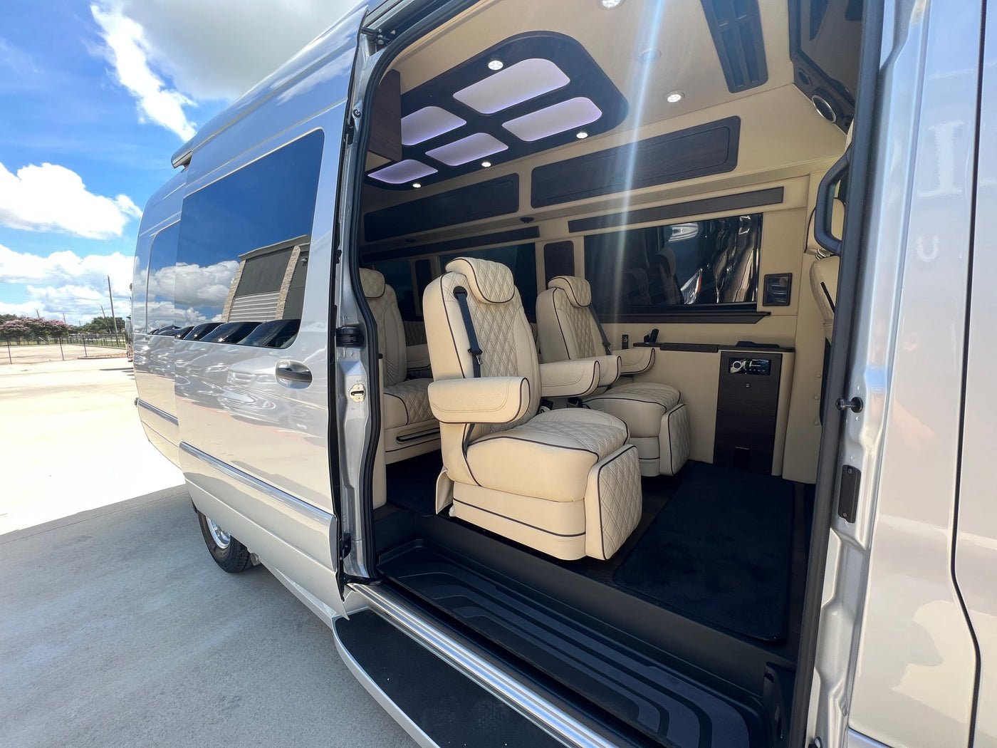 Experience a luxury RV rental. This spacious van's interior features cream, quilted seats, ambient lighting, and dark wood accents. — photo 3