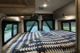 Cozy rv rental bedroom features a geometric blue/white quilt, panoramic windows, and storage for road trip comfort.