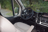 Inside an rv rental, featuring the cockpit with a Ram steering wheel, dashboard, gear shift, and serene natural view.