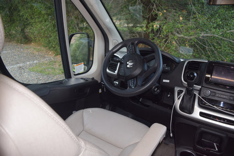 Inside an rv rental, featuring the cockpit with a Ram steering wheel, dashboard, gear shift, and serene natural view.