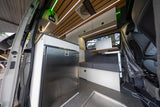 Inside a modern rv rental: a well-equipped kitchen with fridge, comfy bench seating, and a practical laptop desk.
