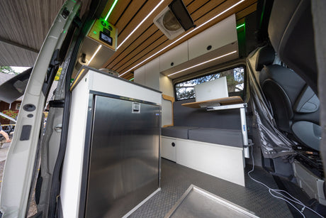 Inside a modern rv rental: a well-equipped kitchen with fridge, comfy bench seating, and a practical laptop desk.