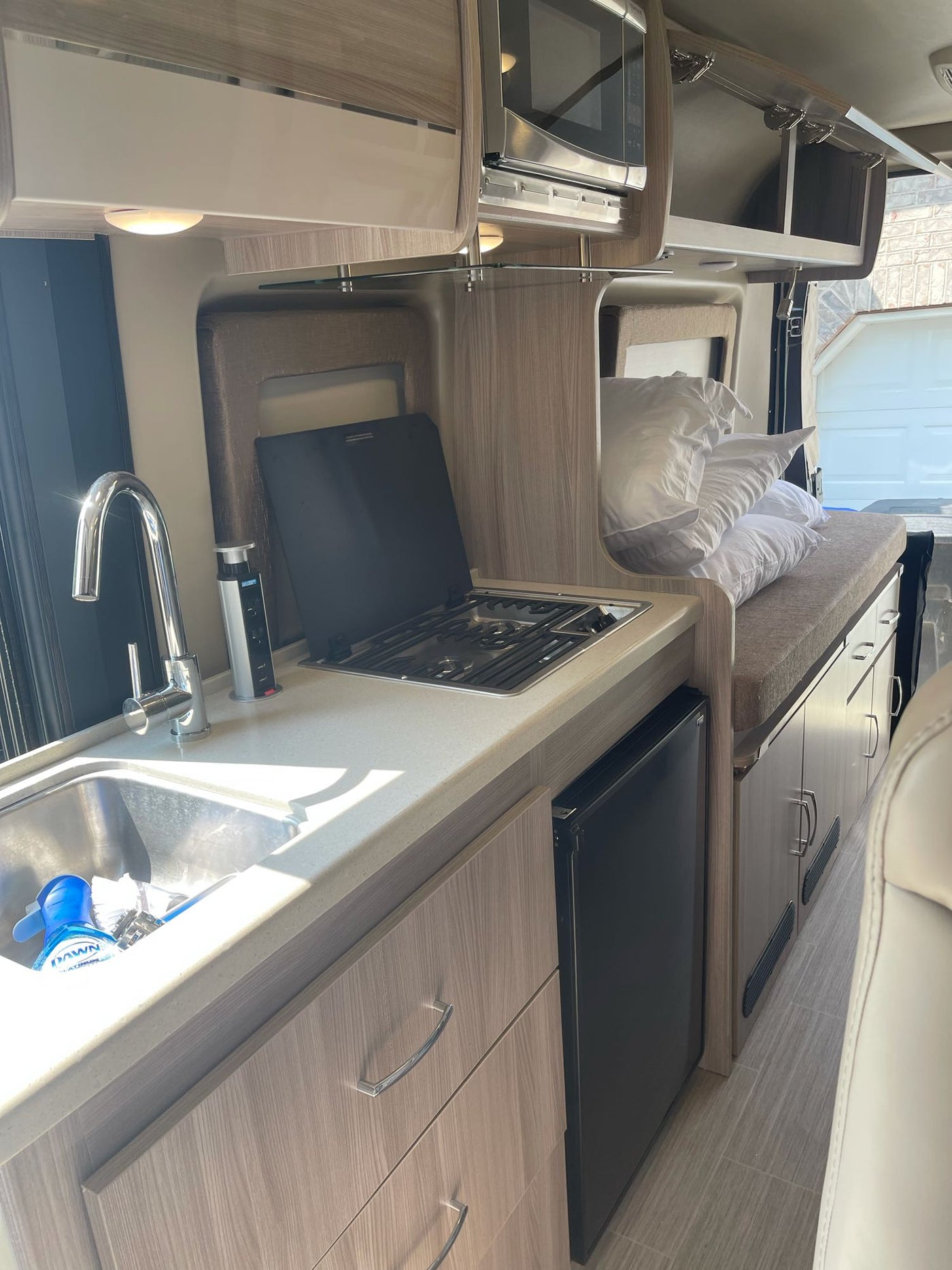 RV rental interior showcasing a compact kitchen with sink/stove, overhead microwave, and a cozy sleeping area. — photo 13