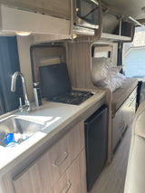 RV rental interior showcasing a compact kitchen with sink/stove, overhead microwave, and a cozy sleeping area.