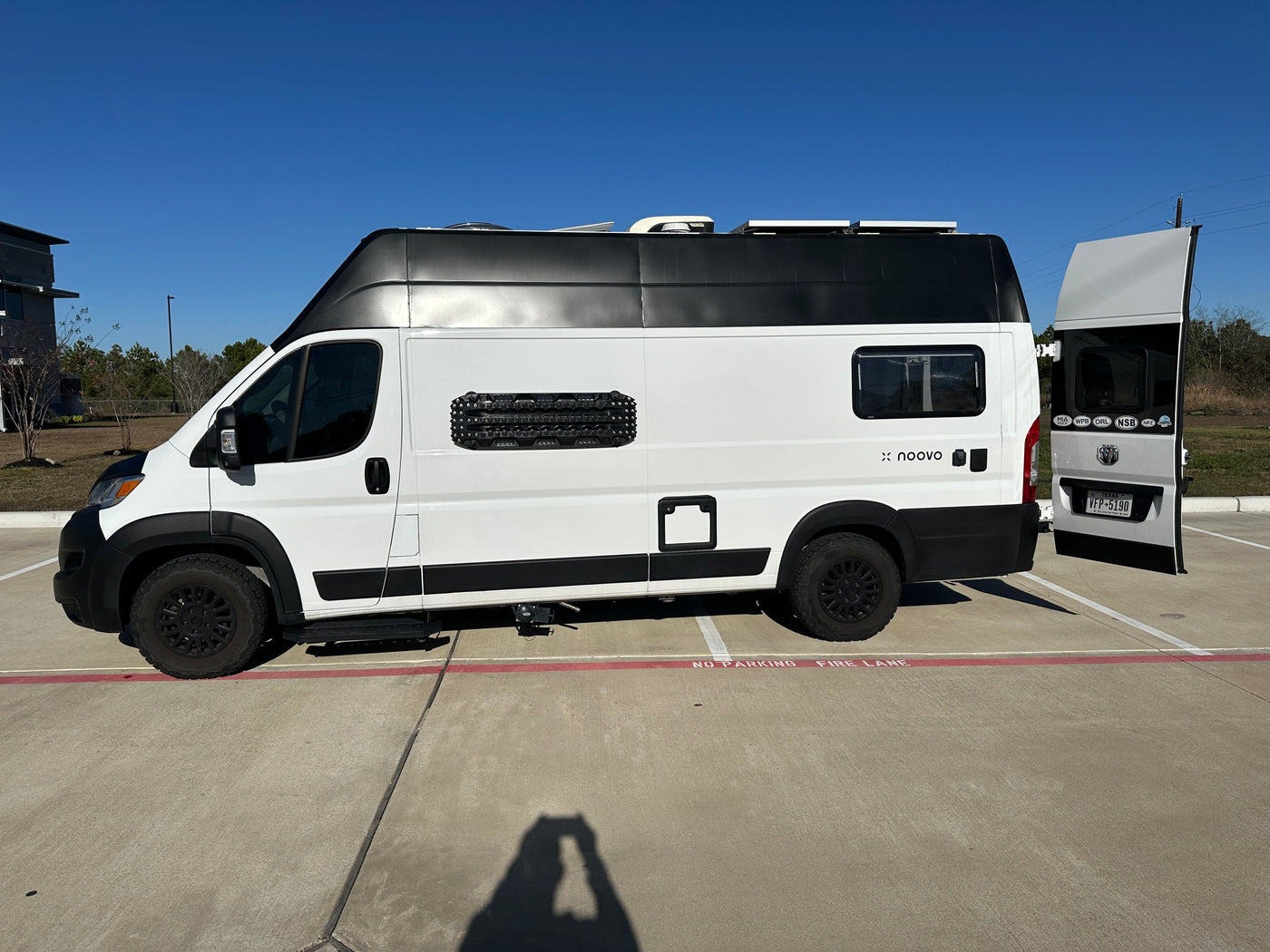 A white and black noovo rv rental camper van, equipped for adventure, is parked on concrete, partially in a fire lane. — photo 6