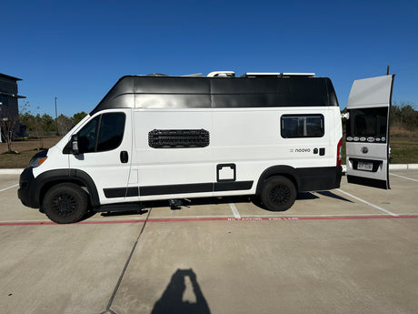 A white and black noovo rv rental camper van, equipped for adventure, is parked on concrete, partially in a fire lane.