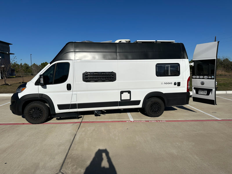 A white and black noovo rv rental camper van, equipped for adventure, is parked on concrete, partially in a fire lane. — photo 6