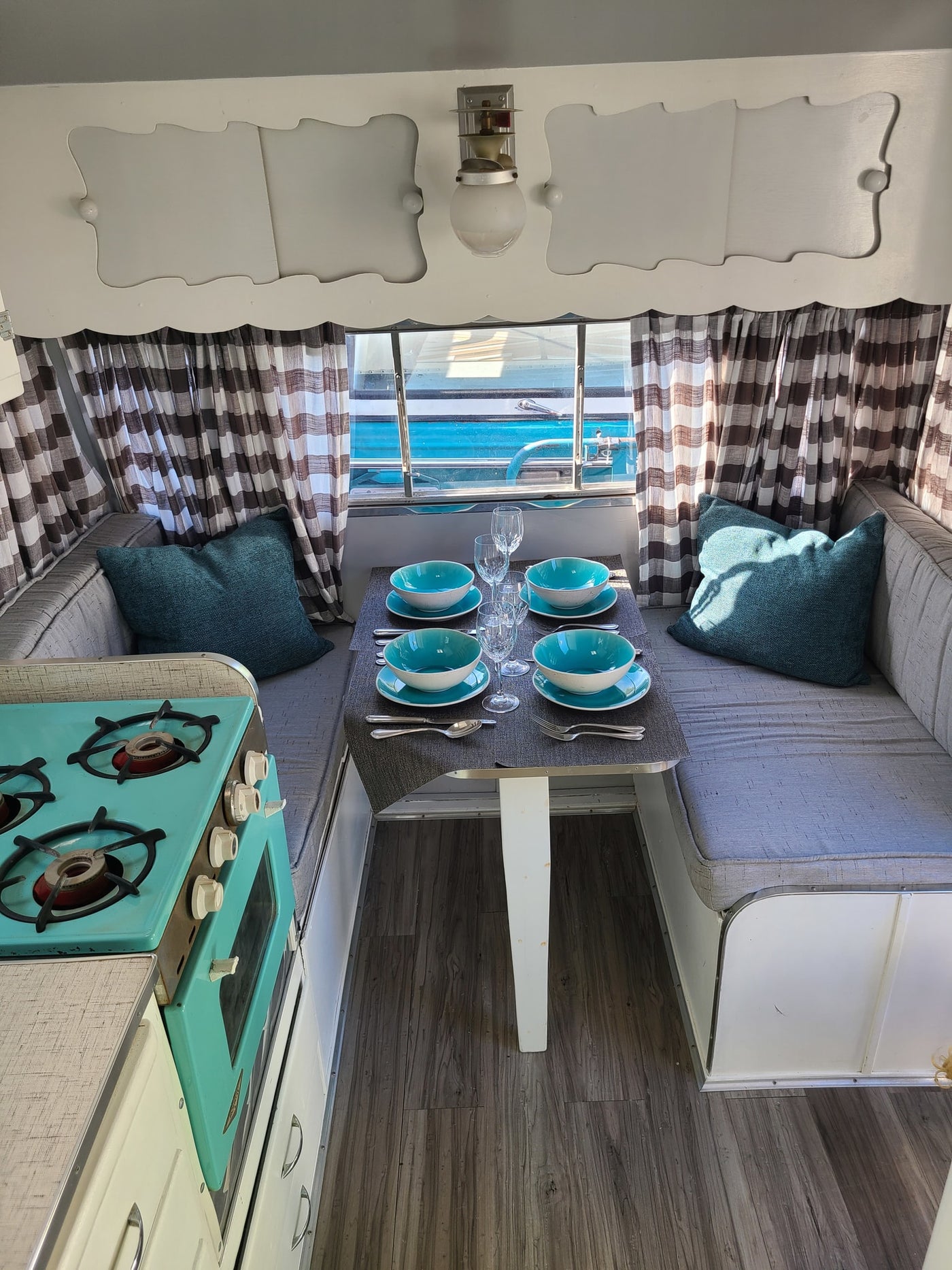 Cozy vintage RV rental interior with a teal kitchen stove, set dinette, comfy bench seating, and charming checkered curtains. — photo 8