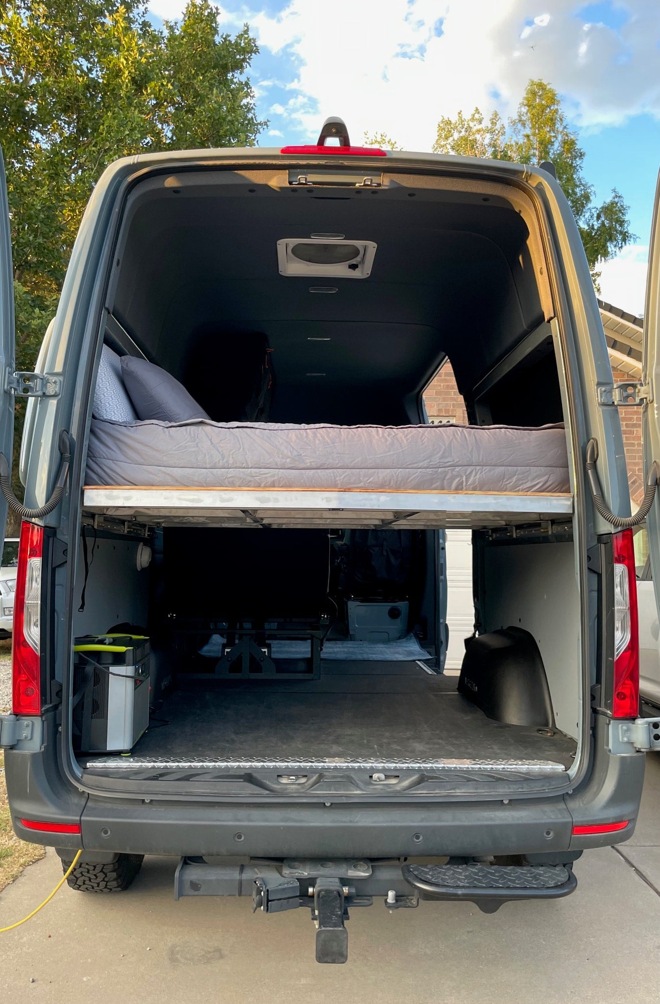 View of a gray RV rental camper van's interior, showcasing a raised bed and spacious storage area below. — photo 20