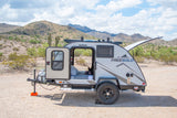 This RV rental teardrop camper is set up in a scenic desert landscape, perfect for outdoor adventure with a dog inside.