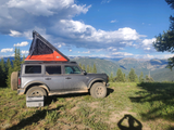 Overlanding setup: a dirty Ford Bronco with rooftop tent overlooks mountains. Great for an **RV rental** adventure & off-grid camping!
