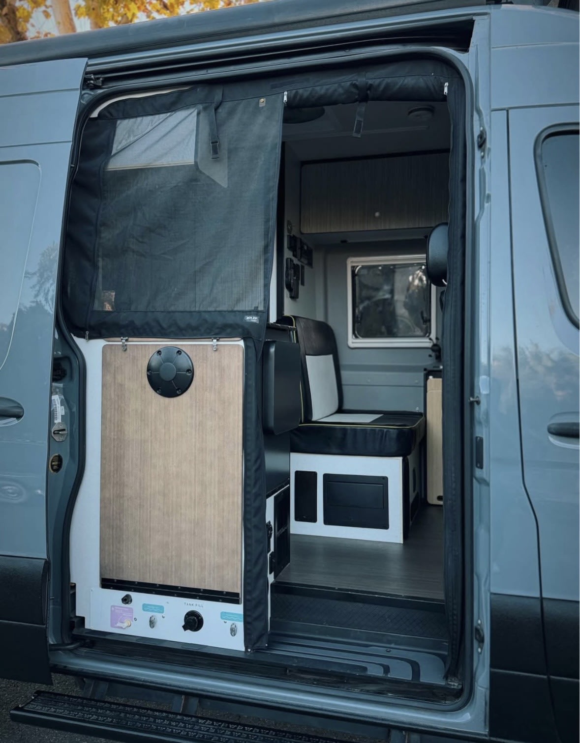 Inside an RV rental: a detailed view of its open side door with a mosquito net, custom water/gas panel, and comfortable seating. — photo 9