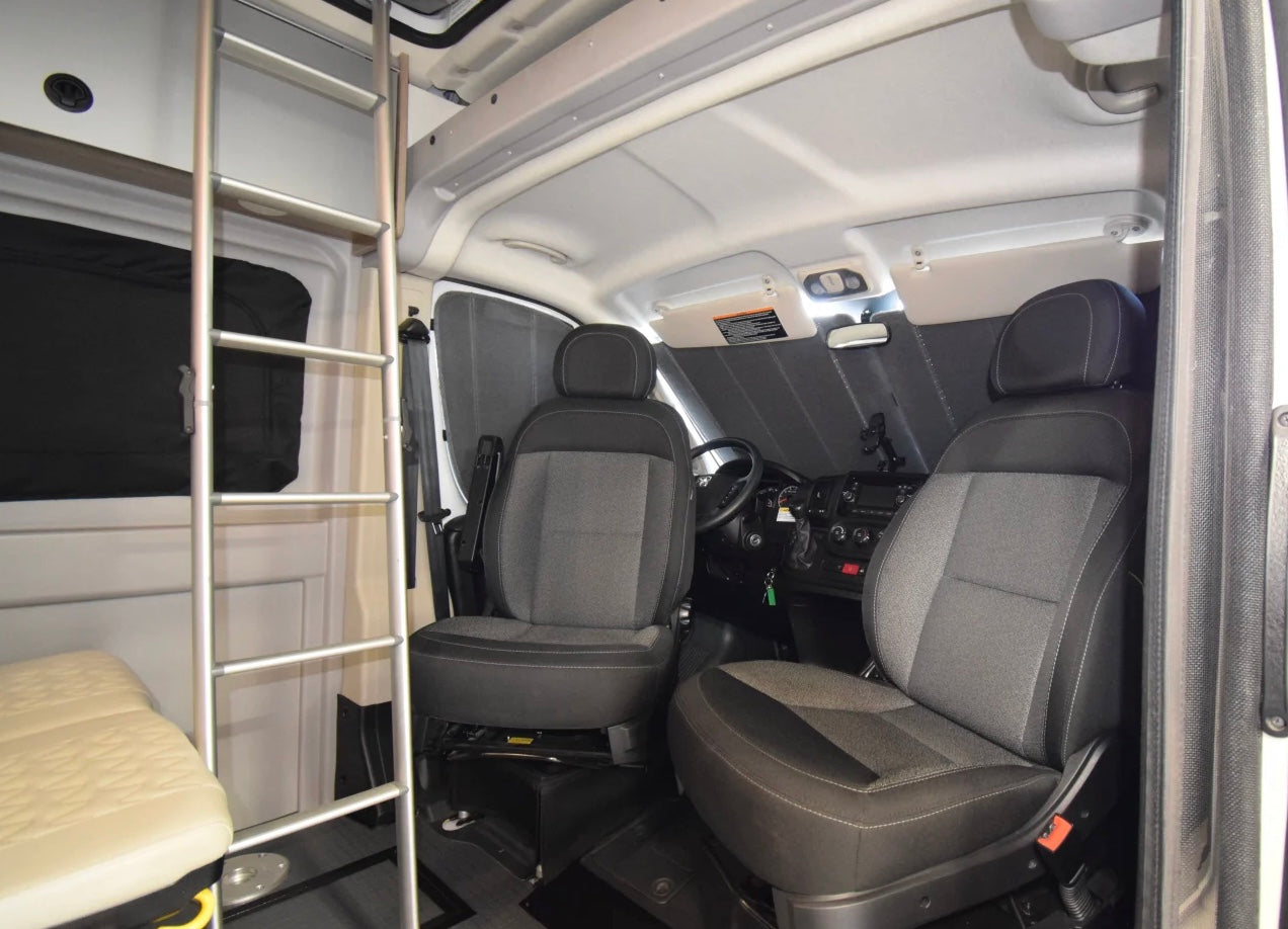 RV rental: Interior of a camper van's front cabin, showing driver/passenger seats, dashboard, and a ladder to an upper bunk.