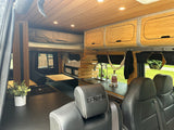 Sleek wood-paneled RV rental interior featuring a kitchen, elevated bed, and front seating.