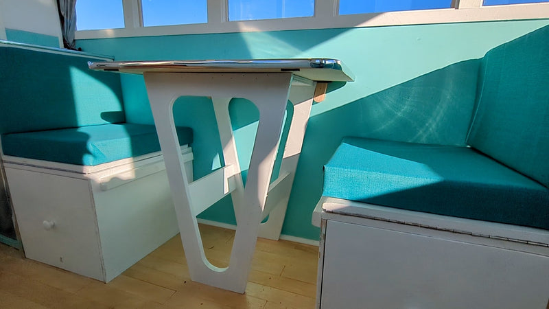 Sunny RV rental dinette features a white V-shaped table, teal cushions, and under-seat storage, brightly lit by windows. — photo 5