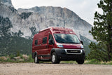 Red camper van for RV rental, parked on a mountain dirt road, surrounded by nature and evergreen trees.