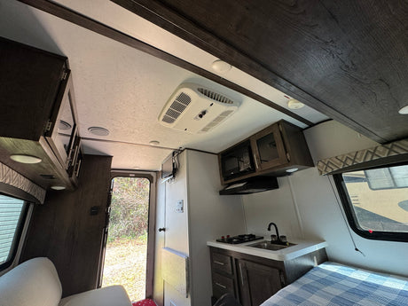 Interior of an rv rental, featuring a compact kitchen, bed, and an open door to the outside. Bright, functional living space.