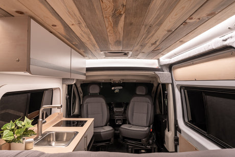 Inside a cozy rv rental, showcasing its wooden ceiling, equipped kitchenette, and comfortable front cabin setup.