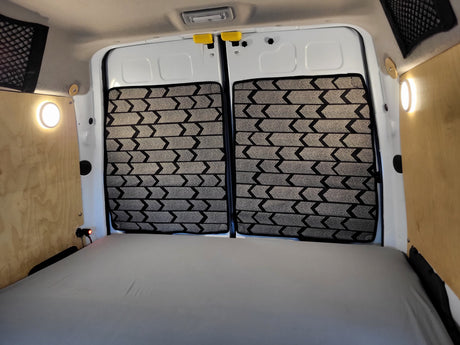 Spacious RV rental camper van interior: bed, custom patterned rear door window covers, and practical lighting on wood panels.