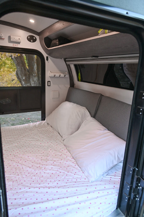 RV rental interior: A cozy bed with pink polka-dot sheets, white pillows, and overhead storage awaits adventurers.