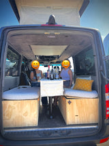 Two women enjoying wine inside a custom camper van rv rental. The van features a built-in table, beds, & storage, with an open rear for views.