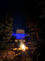 Cozy night camping under the stars with an RV rental truck camper & glowing campfire. Blue light inside camper.