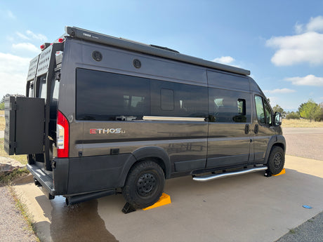 This dark gray Ethos Li camper van rv rental is parked with yellow leveling blocks. It features a Thule awning and rear cargo.