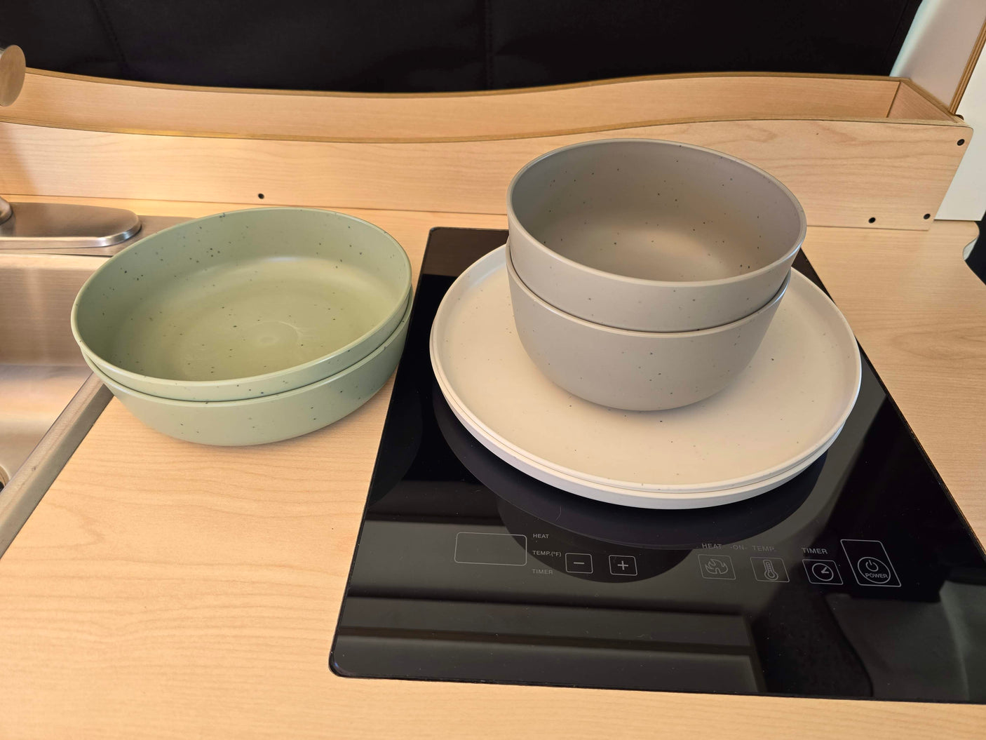 An RV rental's well-appointed kitchenette features an induction cooktop, sink, and dishes, perfect for compact living.