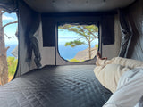 Relaxing in an RV rental's cozy rooftop tent, offering stunning ocean and cliff views. A perfect nature escape.