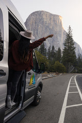 El Capitan views from an RV rental. A person in a hat reaches out of a parked van on a Yosemite road trip.