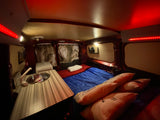 Cozy camper van interior, perfect for an RV rental, featuring a comfortable bed, compact kitchen with sink, and ambient red and white lighting.