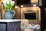 This inviting RV rental interior features a chic kitchen area with white tulips and comfortable seating.