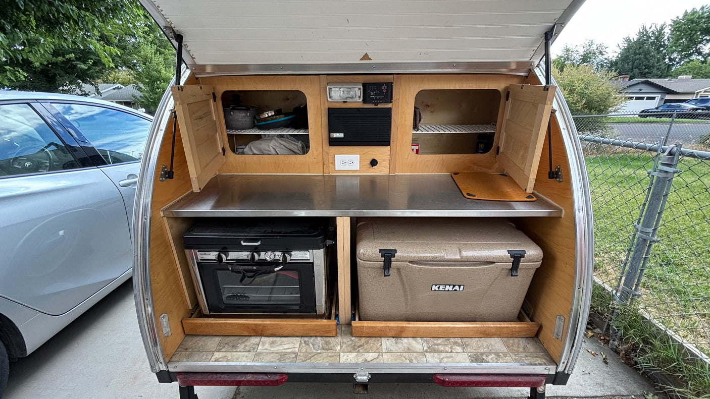This teardrop trailer galley, perfect for rv rental, features an outdoor kitchen with oven, cooler, storage, and stainless steel counter.