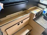 Inside an RV rental: open wooden storage compartments, black panels, and a counter with a battery notice, showing efficient interior design.