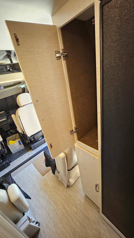RV rental interior features: an open light-colored cabinet with a dark felt lining, adjacent to a dark appliance, near cabin seating.