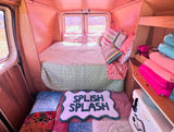 Explore this charming rv rental's interior: a comfy bed, pink walls, colorful towels, and a fun "Splish Splash" mat.