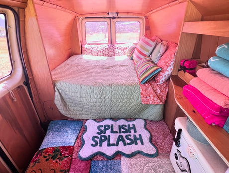 Explore this charming rv rental's interior: a comfy bed, pink walls, colorful towels, and a fun "Splish Splash" mat.