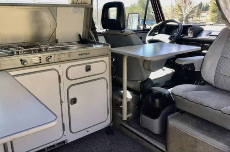  amidst vibrant green aloe plants with red flowers under blue sky.|Inside this RV rental: view of the driver's cabin with steering wheel and front seats.|Interior of an RV rental: view of a gray patterned bench seat — photo 6